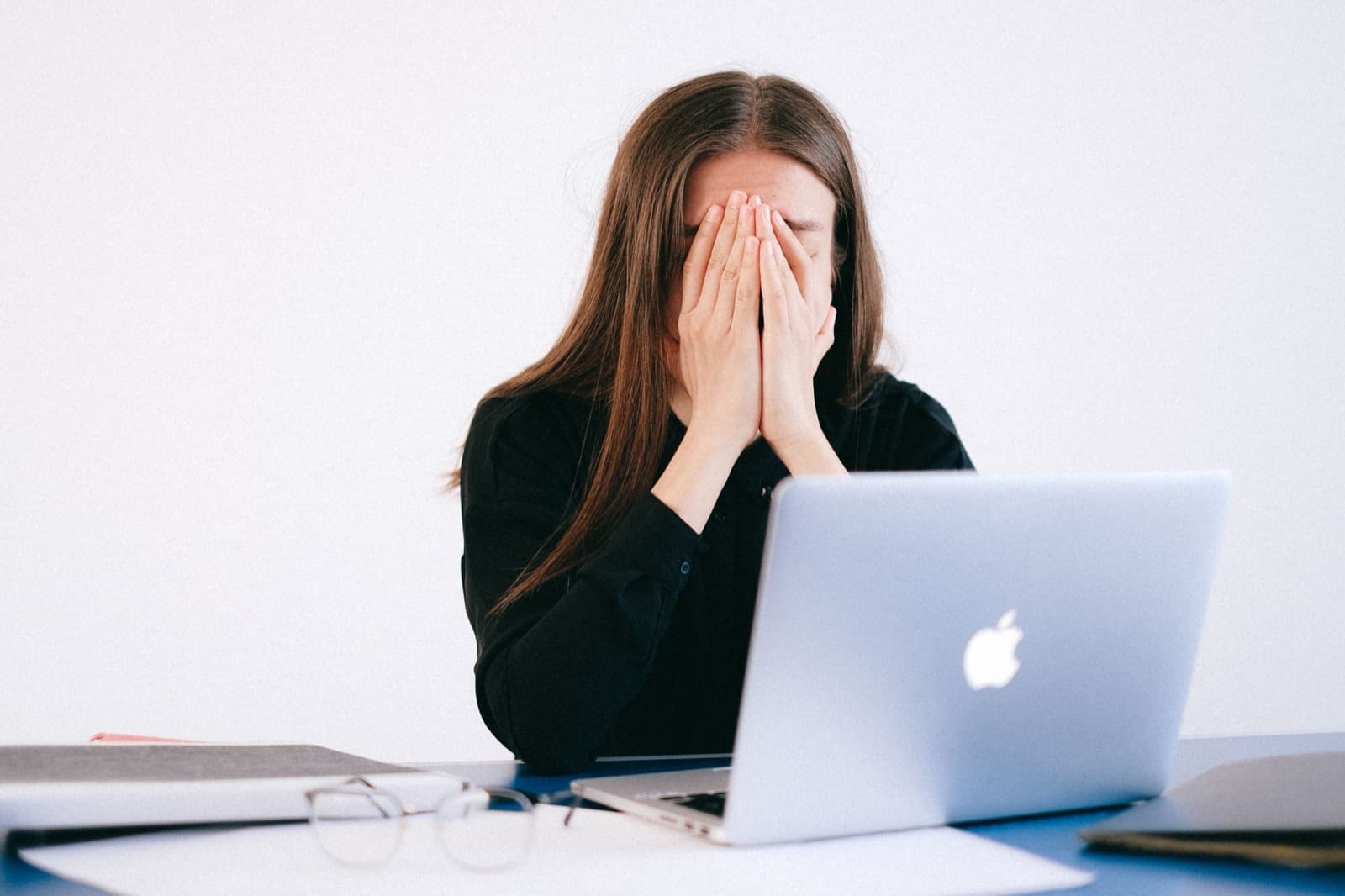 A student at a laptop with her face in her hands, stuck on her college essay