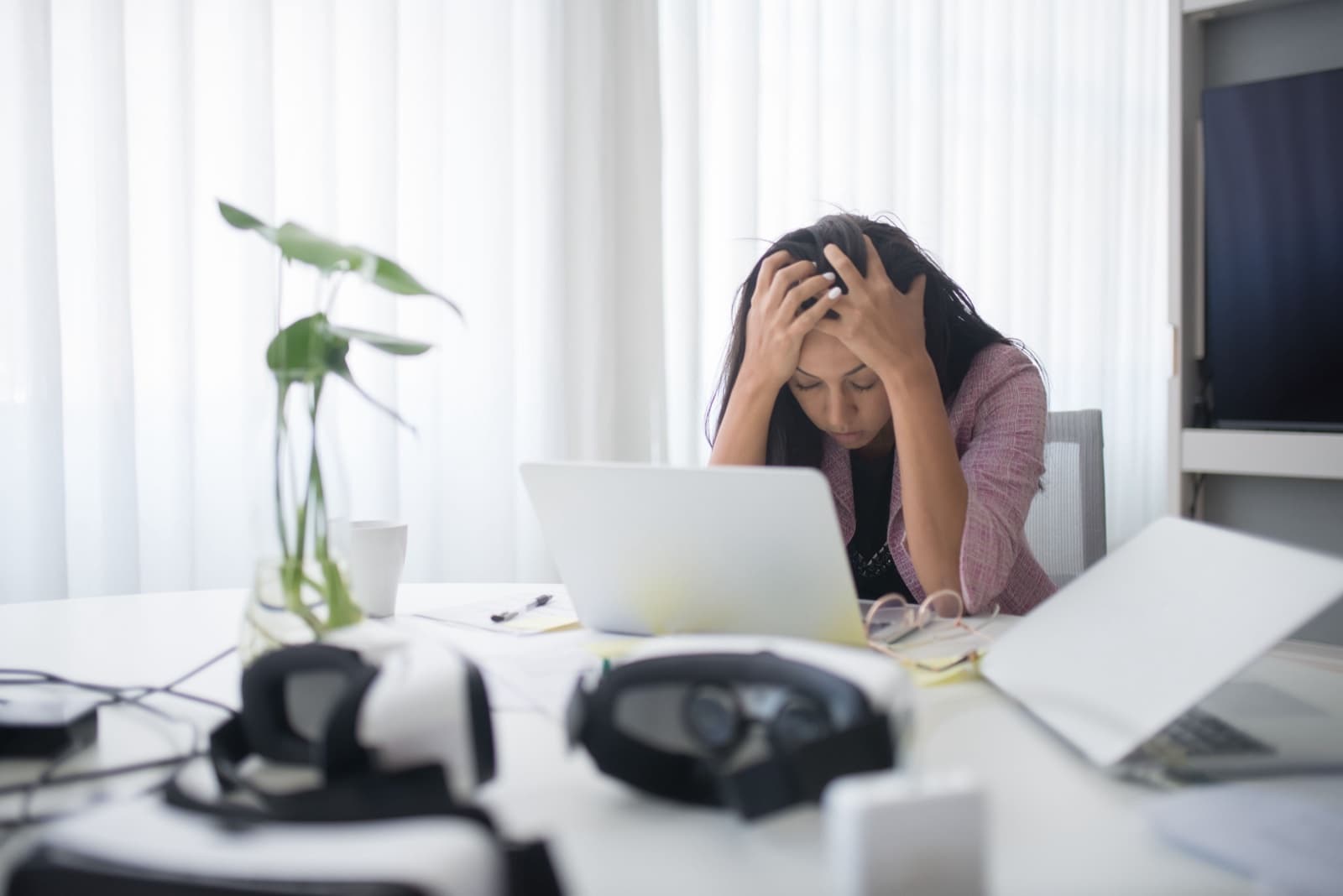 A student holding her head at a desk, overwhelmed by a laptop and paperwork
